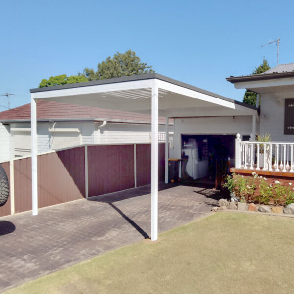 White DIY freestanding flat roof carport beside a home with blue sky.