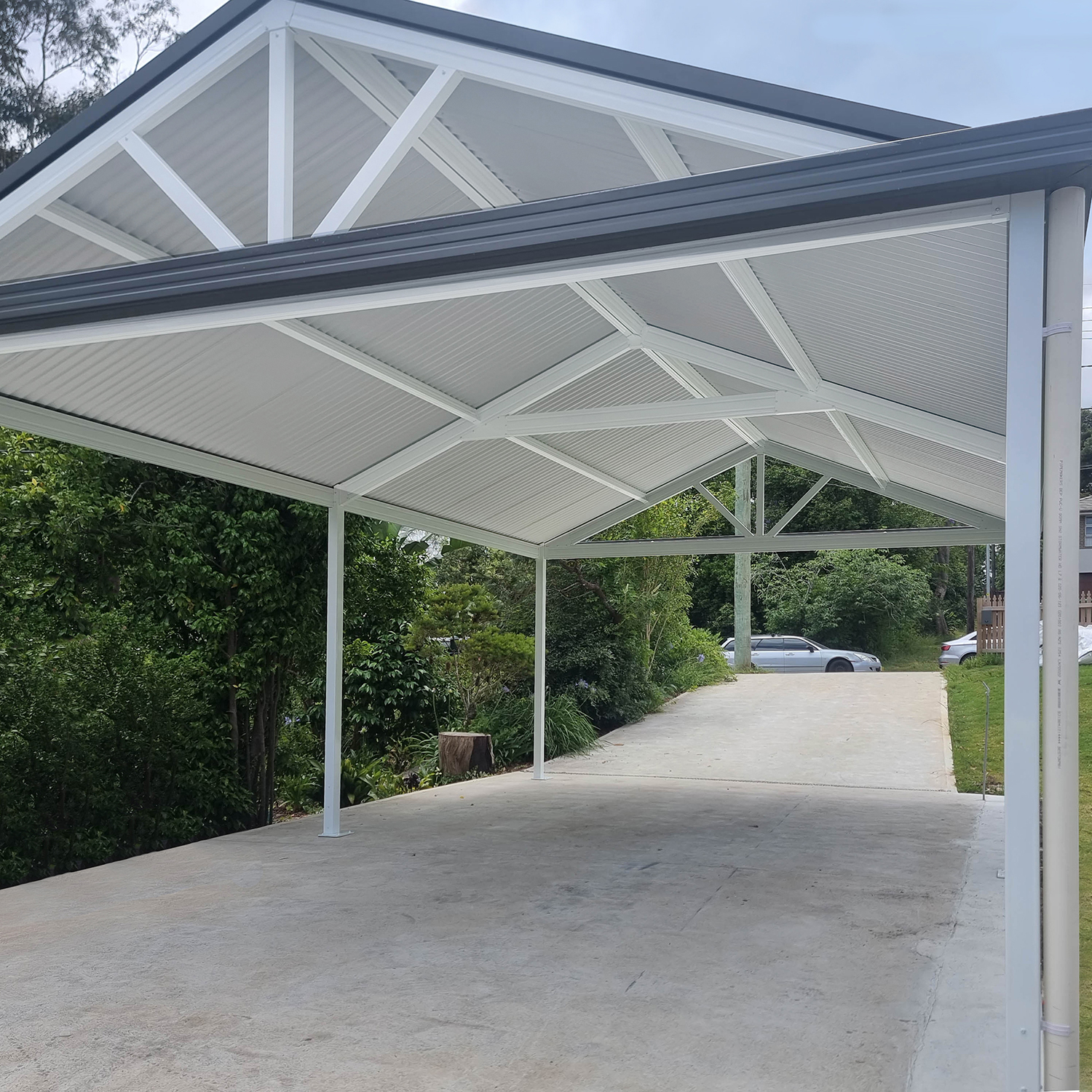 Modern diy freestanding gable roof carport with driveway in green outdoor setting.