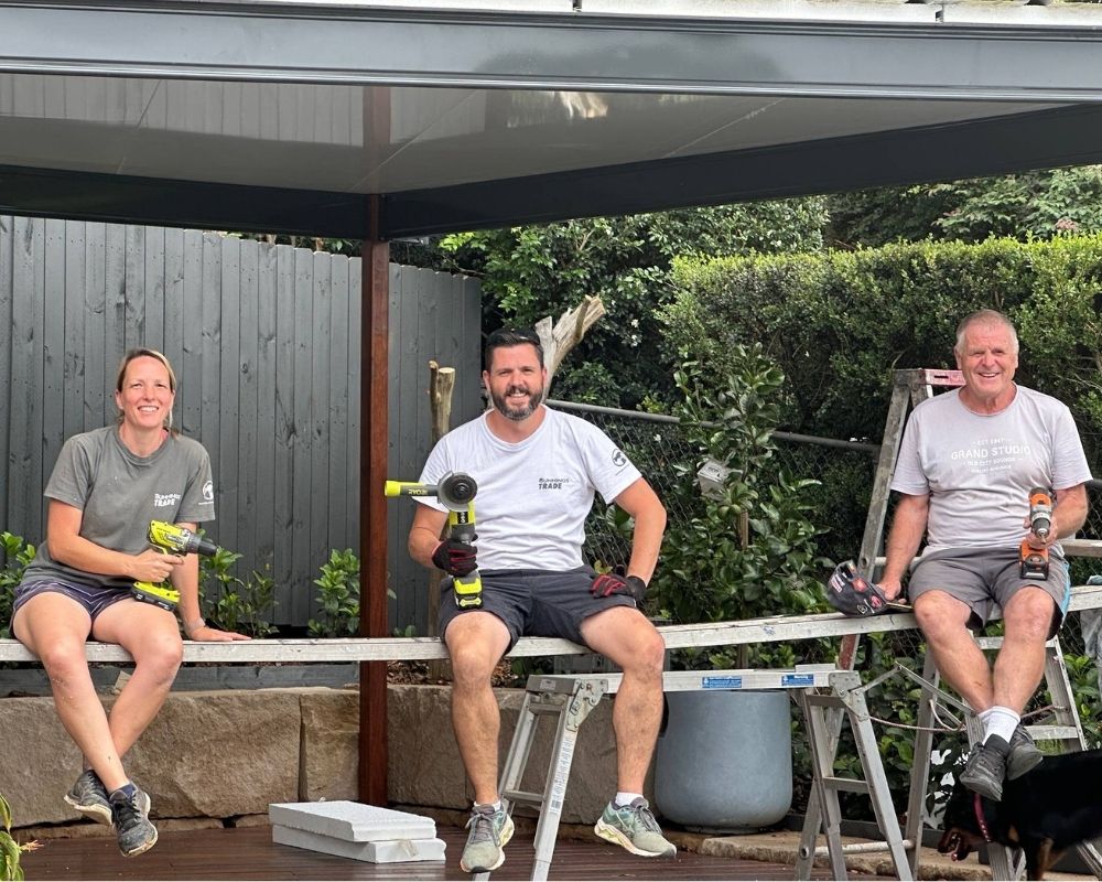 Three tradespeople seated with tools outdoors.